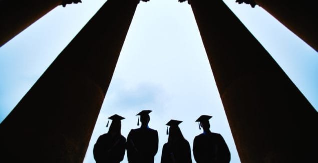 Image of 4 college student grads with commencement caps on in silhouette