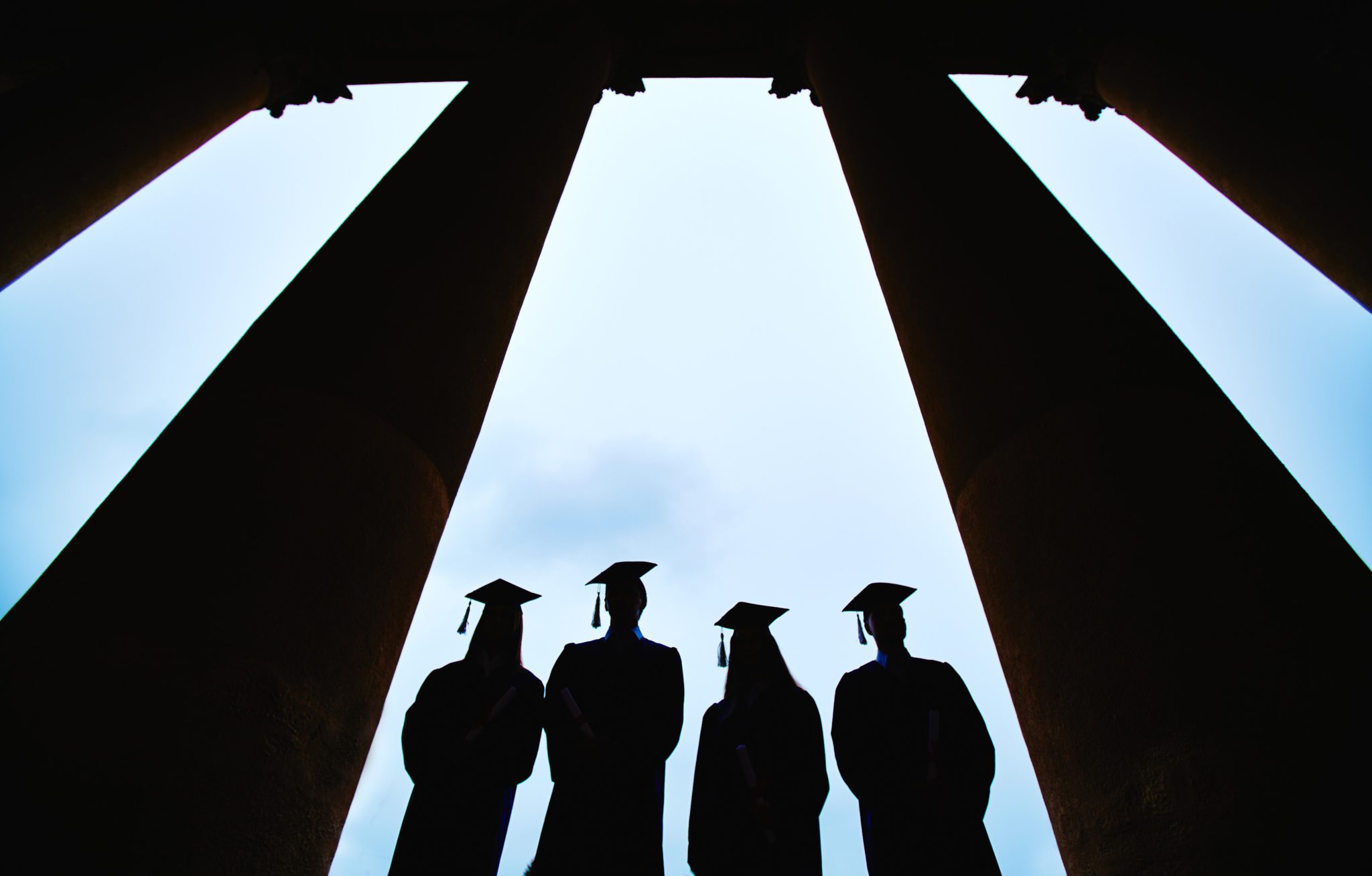 Image of 4 college student grads with commencement caps on in silhouette