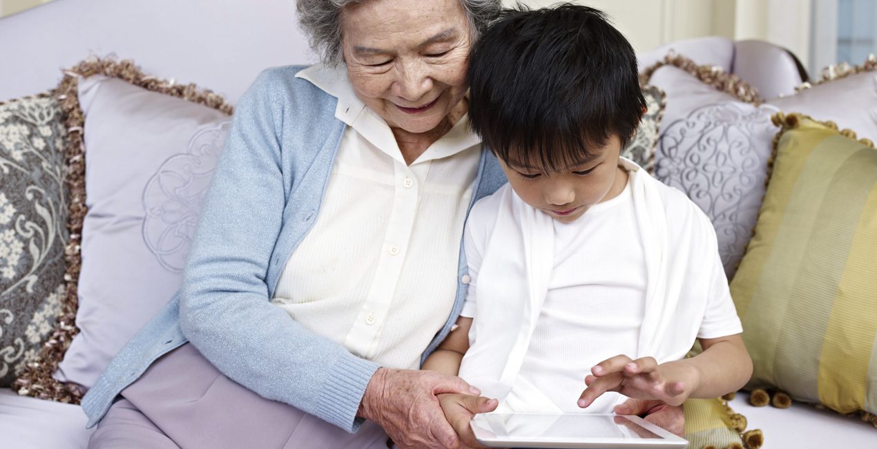 autism and technology concept - grandmother helping grandson with tablet