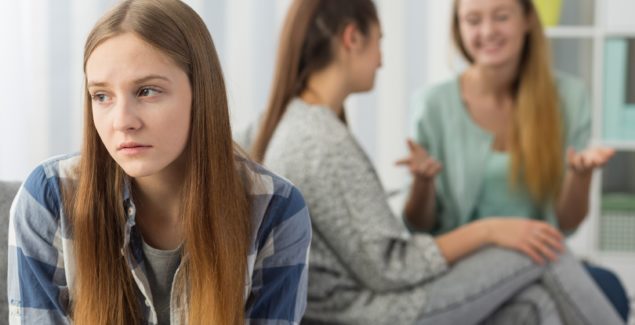 Image of a girl on her own while two others chat happily