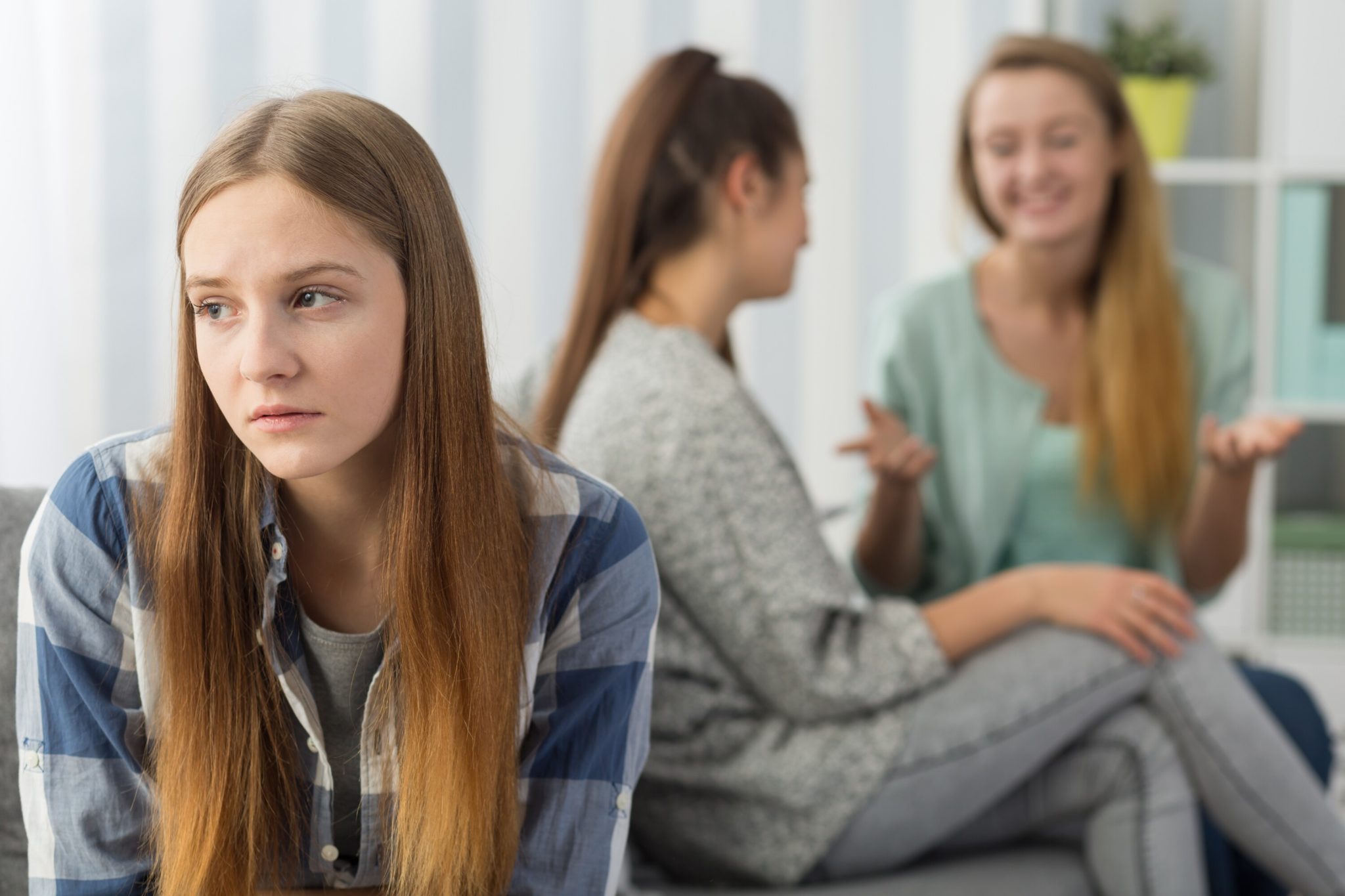 Image of a girl on her own while two others chat happily