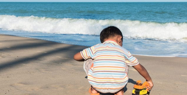 Cute little boy play toy car on the beach alone