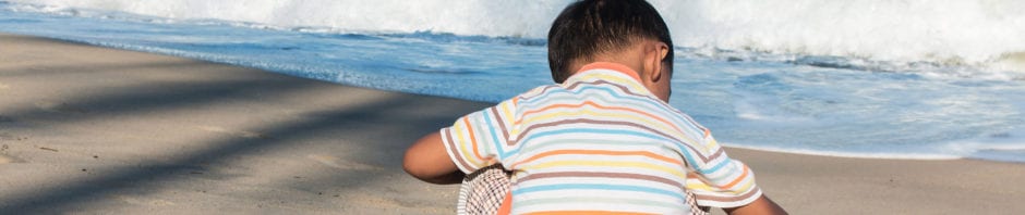 Cute little boy play toy car on the beach alone