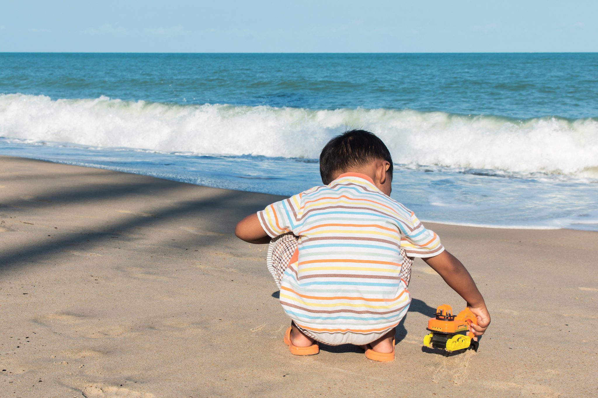 Cute little boy play toy car on the beach alone