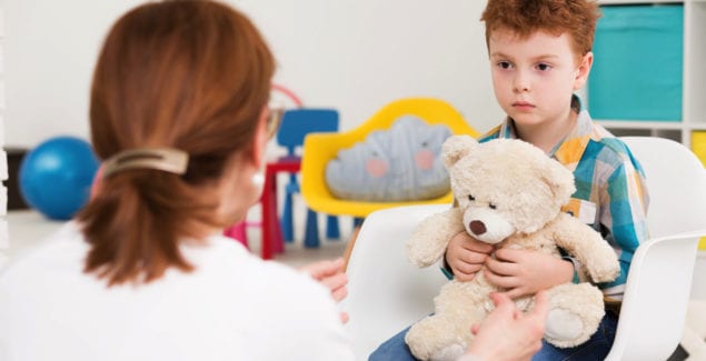 Red-haired, autistic boy with teddy bear concentrated on his therapist