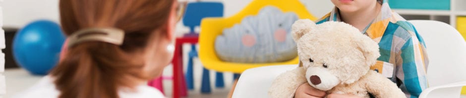 Red-haired, autistic boy with teddy bear concentrated on his therapist