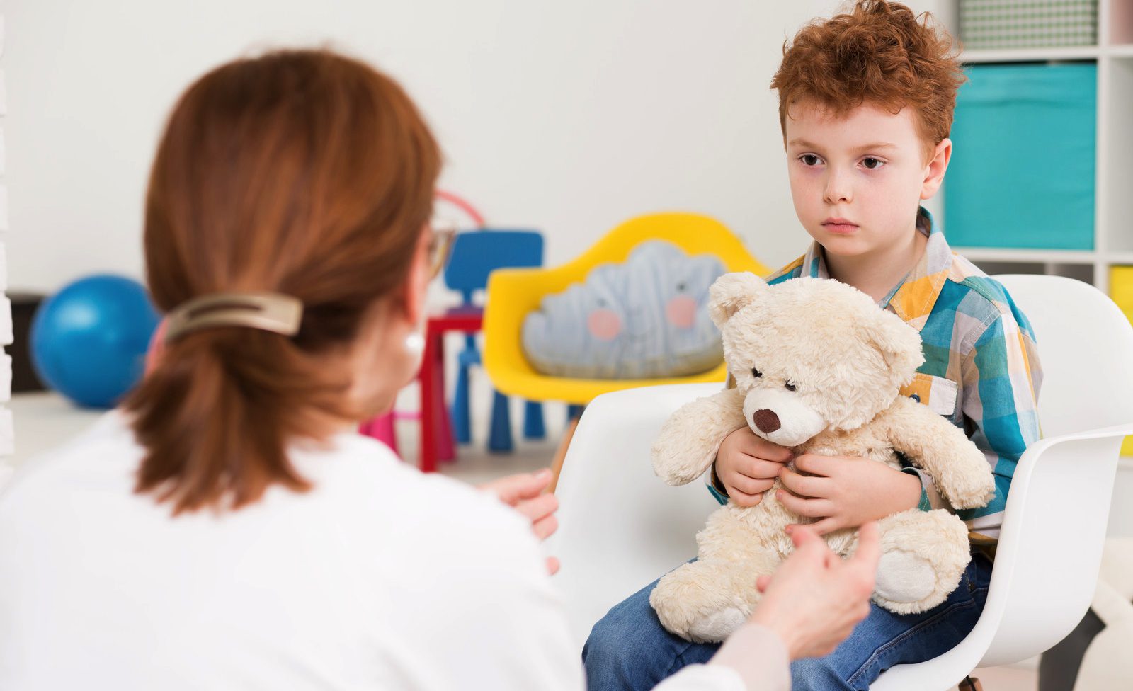 Red-haired, autistic boy with teddy bear concentrated on his therapist