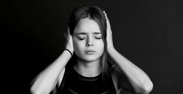 Black and white image of young teen girl closing her eyes and covering her ears with her hands