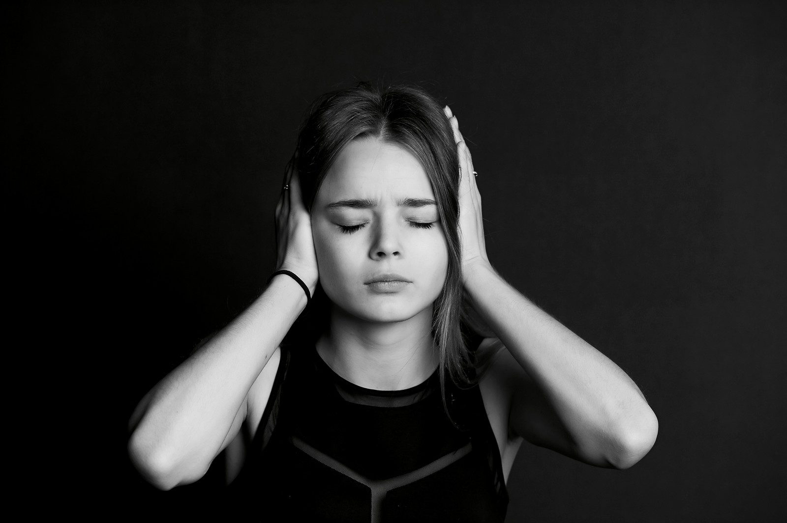 Black and white image of young teen girl closing her eyes and covering her ears with her hands