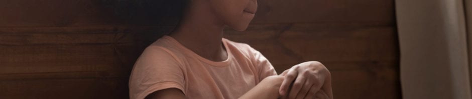 high functioning autism concept - Pensive african preschool or school age girl sitting on floor alone, leaned on wooden wall puts hands on laps looking away
