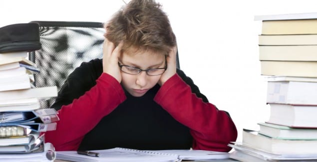 attention deficit - boy sitting at desk piled with books