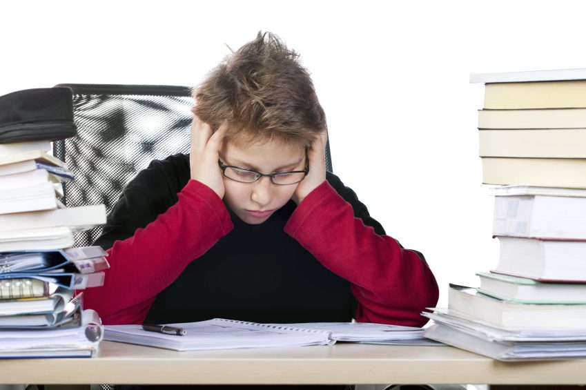 attention deficit - boy sitting at desk piled with books