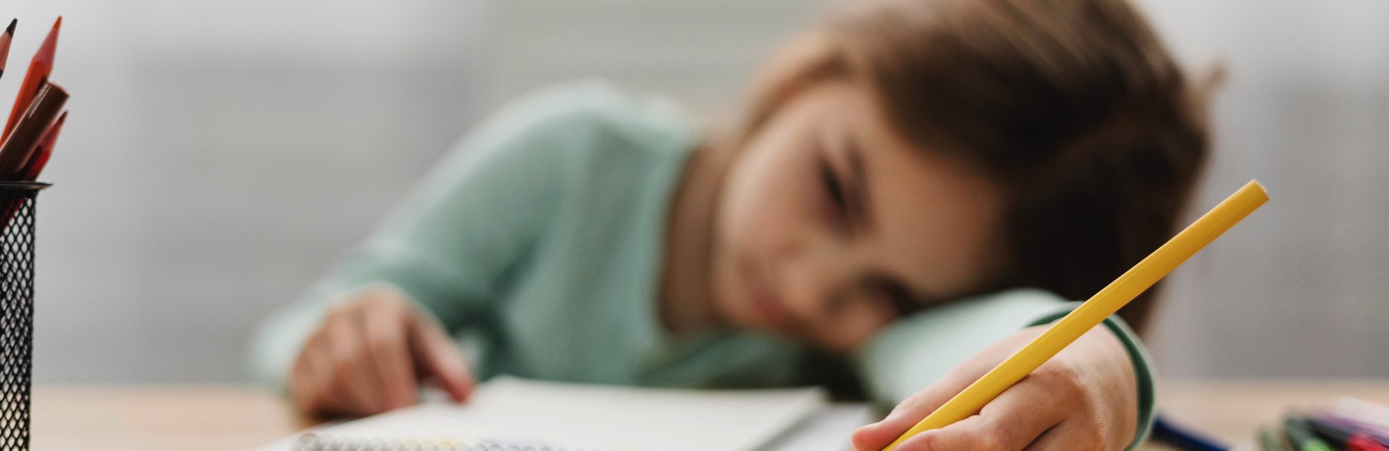 Sad girl resting head on desk with pencil in hand