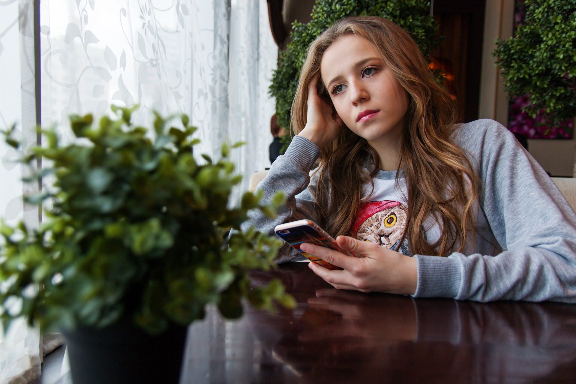 Sad girl sitting at a table holding her phone