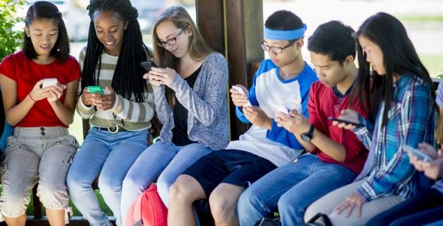 A multi-ethnic group of high school teenagers are sitting outside and are texting on their cell phones before class.