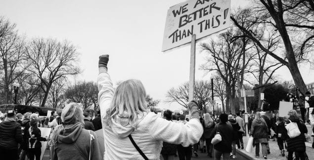 woman holding sign reading "we are better than this!"