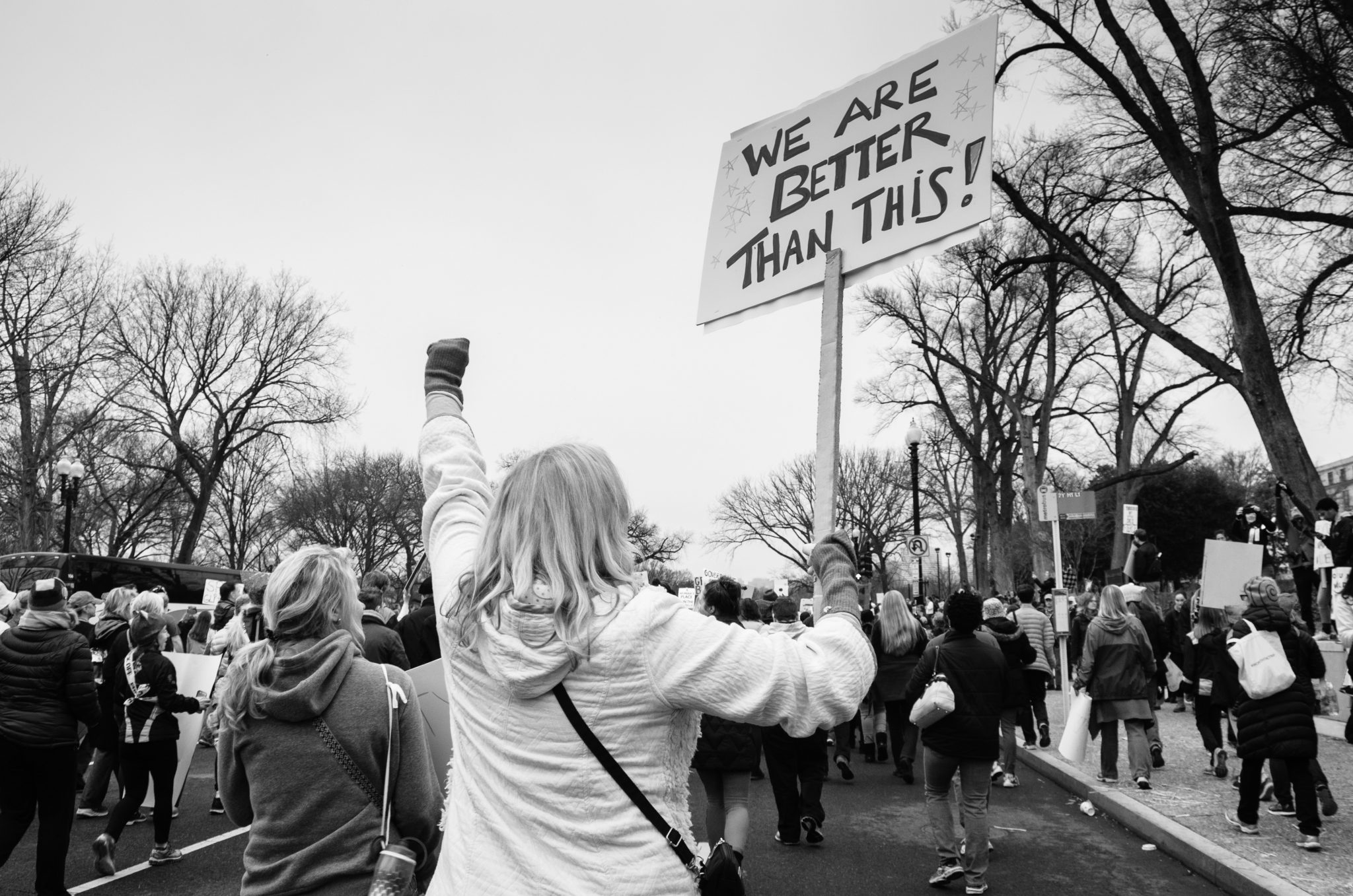 woman holding sign reading "we are better than this!"