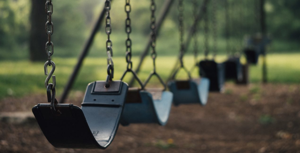 Photo of a row of swings in a playground, all empty