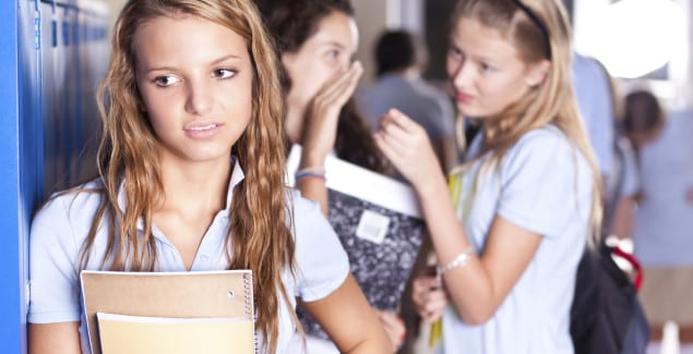 Middle School - Young teen standing at lockers with other teens in the background