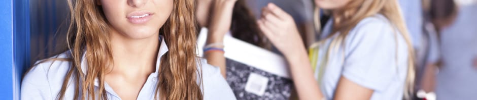 Middle School - Young teen standing at lockers with other teens in the background