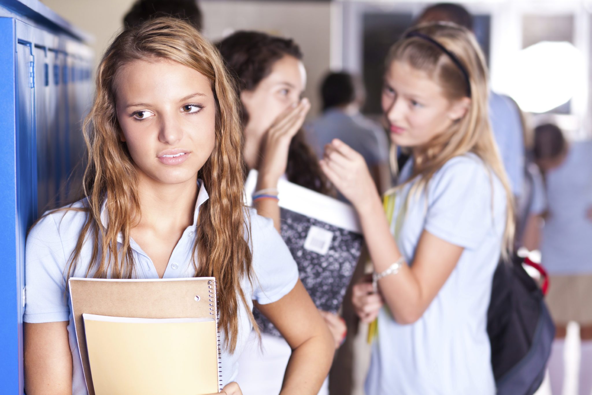 Middle School - Young teen standing at lockers with other teens in the background