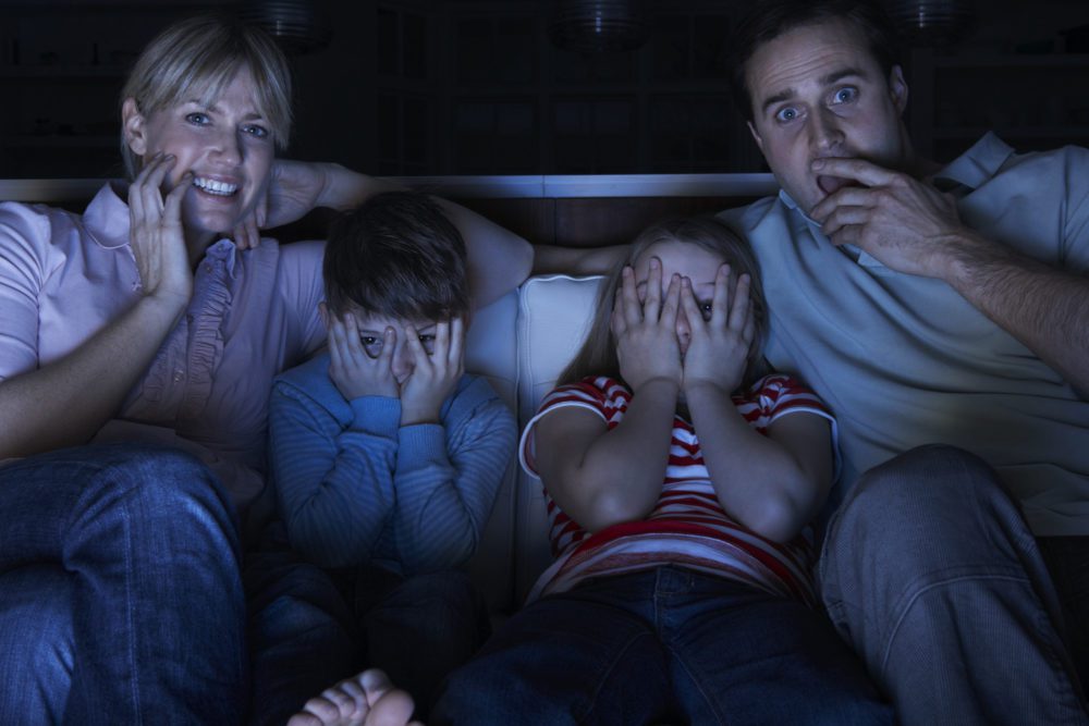 Horror movies - Family sitting on sofa in dark looking scared, watching tv
