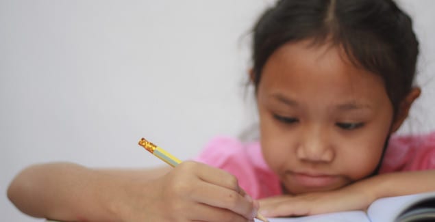 Slow Processing Speed - Close up photo of young girl at desk writing in notebook focusing hard