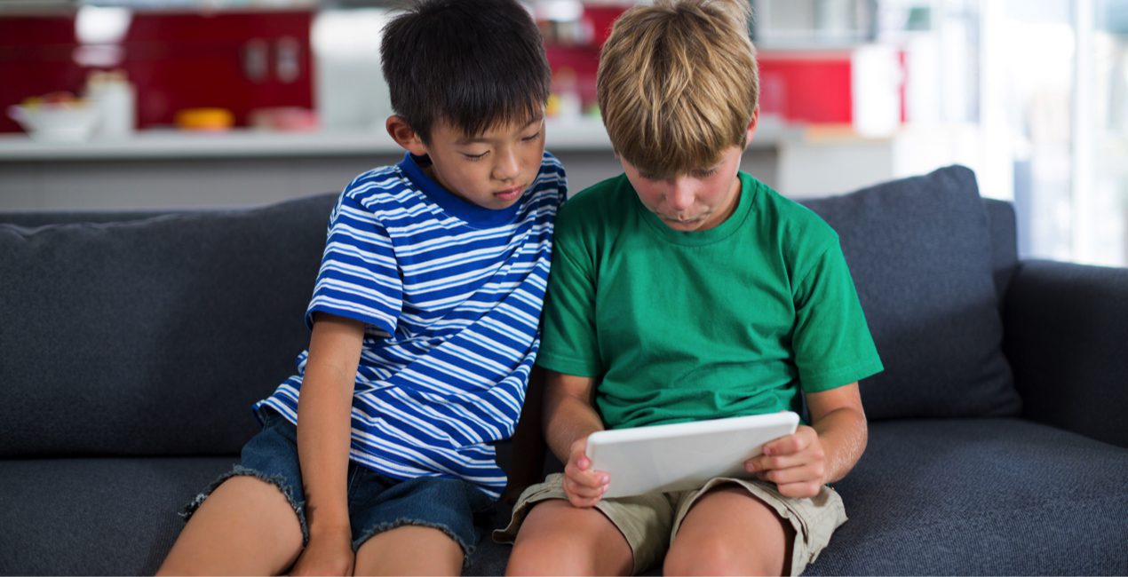 Media literacy - Social Media Mental Health - Two grade school-age siblings using a digital tablet on the couch