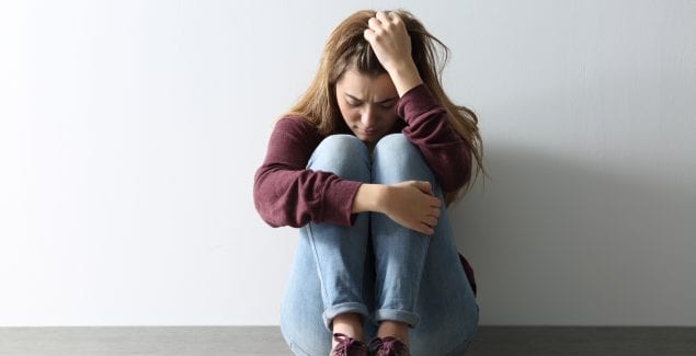 Teen sitting against wall with knees to chest and holding head in hand