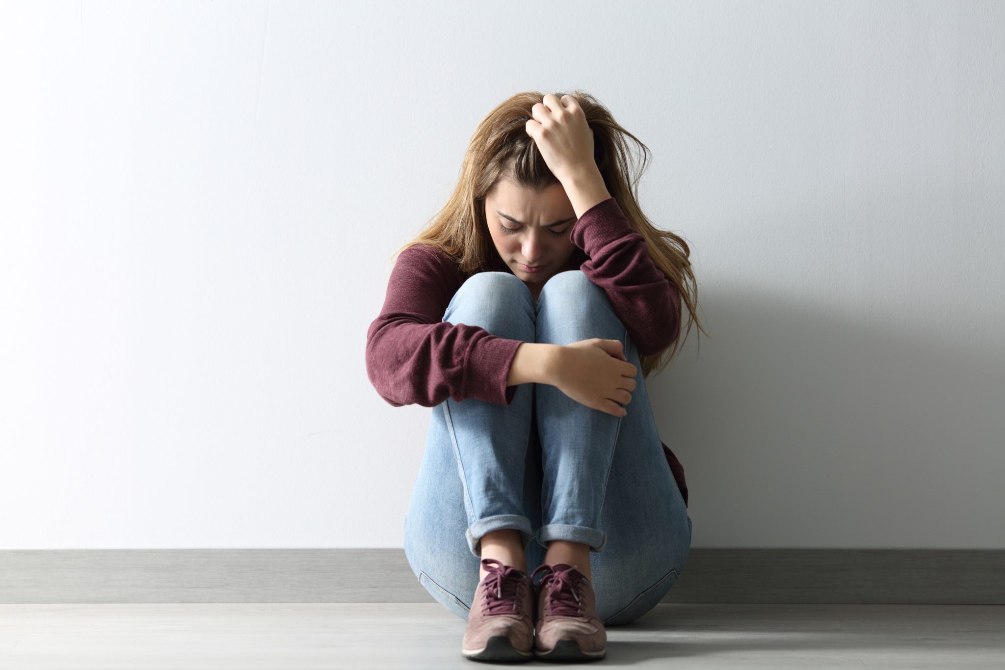 Teen sitting against wall with knees to chest and holding head in hand