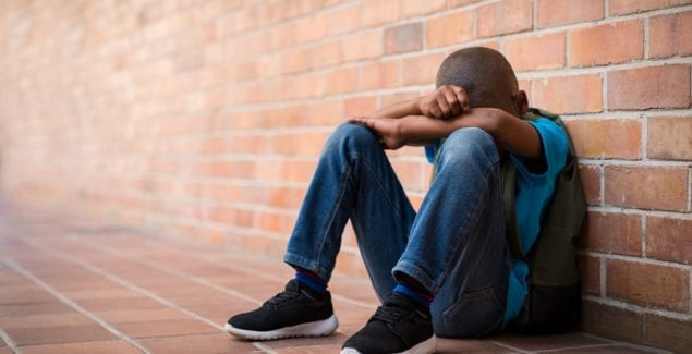 Sad young boy sitting alone on the ground at school