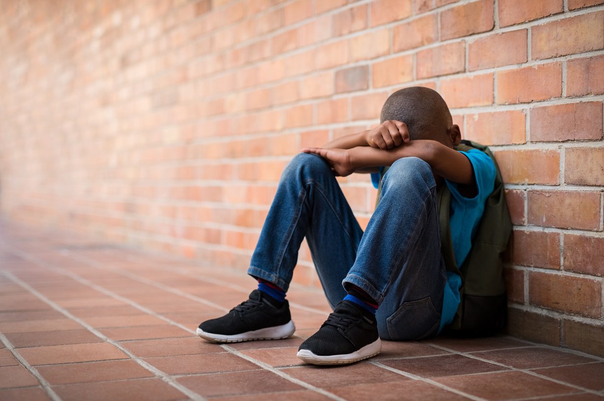 Sad young boy sitting alone on the ground at school